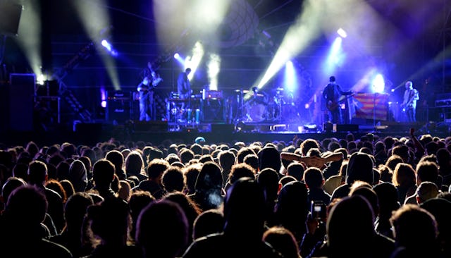 A huge crowd at a One Direction concert with blue spotlights on a stage
