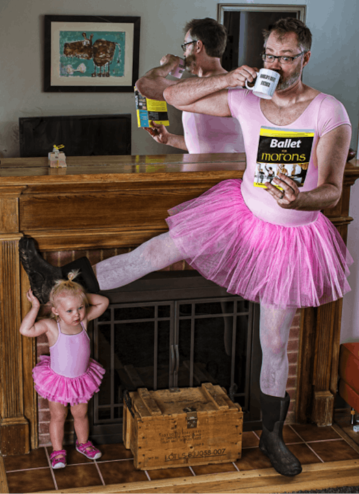 Father and his daughter standing at a fire place while wearing pink ballet dresses with the father r...