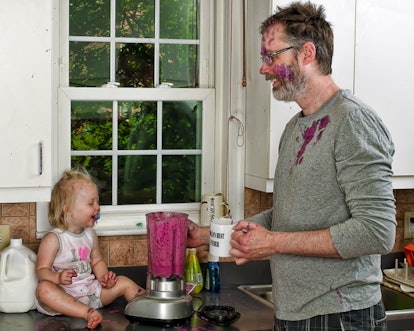 Father and his daughter standing in the kitchen and laughing at the smoothie blender that covered th...