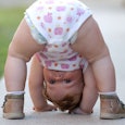 A toddler bending over a looking between her legs on a sidewalk