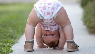 A toddler bending over a looking between her legs on a sidewalk