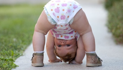 A toddler bending over and looking between her legs on a sidewalk