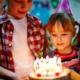 A small girl getting ready to blow out the candles of her birthday cake at her birthday party wearin...