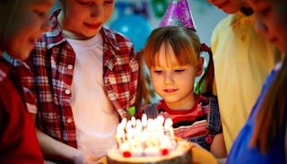 A small girl getting ready to blow out the candles of her birthday cake at her birthday party wearin...