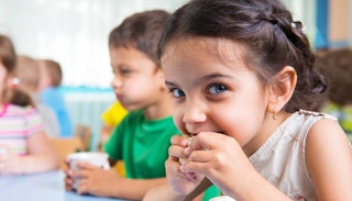 Brown-haired girl biting on a cookie and a little boy with his mouth full behind her