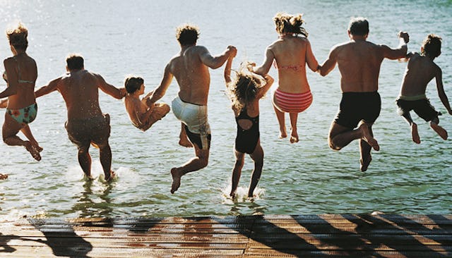 The large family members holding their hands while jumping into the sea.