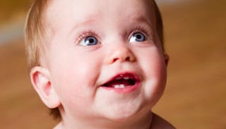 A blonde, blue-eyed toddler, smiling, with his four teeth growing