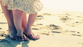 Baby daughter's feet are the parent's feet as they are walking on sand.