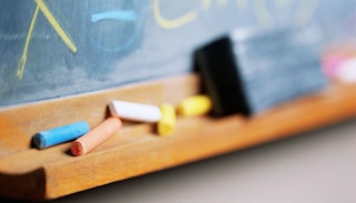 A close-up of pieces of chalk in different colors and a school board with letters written on it