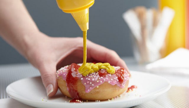  A woman's hand putting mustard on a donut that's already covered with ketchup