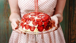 Female hands holding a cake covered with strawberry pieces