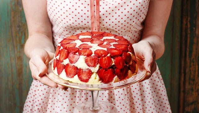 Female hands holding a cake covered with strawberry pieces