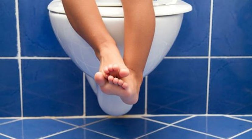 A small kid sitting on a white toilet seat in a bathroom with blue tiles