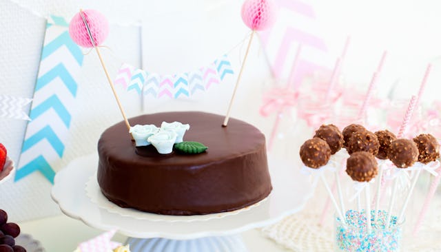 A chocolate cake and sweets for a baby shower with pink and blue decorations behind