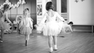 Little girls doing ballet in white dresses in the practice room in black and white