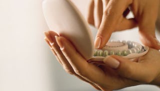 A woman holding a container with birth control pills and taking one out