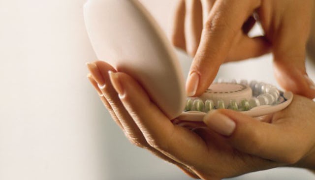 A woman holding a container with birth control pills and taking one out