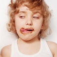A  curly-haired blonde kid eating a chocolate ice cream with the ice cream smeared over its face
