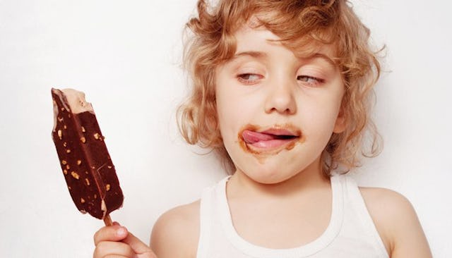 A curly-haired blonde kid eating a chocolate ice cream with the ice cream smeared over its face