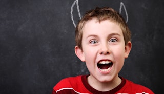 A boy in a red T-Shirt yelling with devil horns drawn onto the blackboard behind him