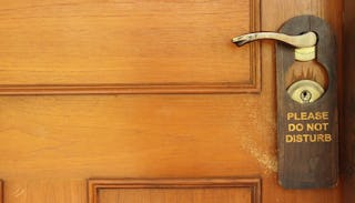 A wooden door with a 'please do not disturb sign' placed by parents so their kids don't catch them i...