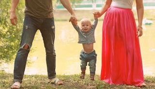 Parents walking with their adopted toddler while holding hands with him on both sides