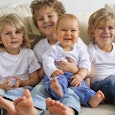 A large family containing four kids wearing the same clothes and sitting on the couch while smiling ...