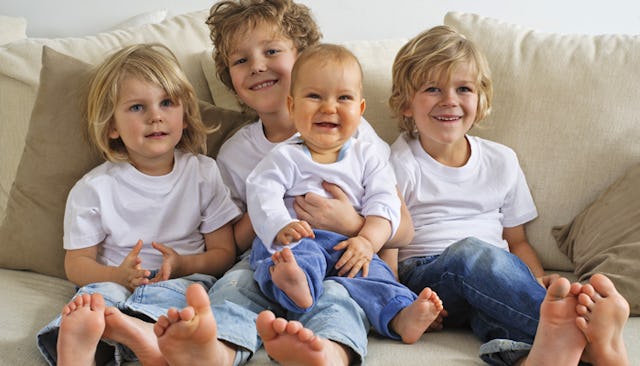 Four siblings wearing the same clothes and sitting on the couch while smiling at the camera