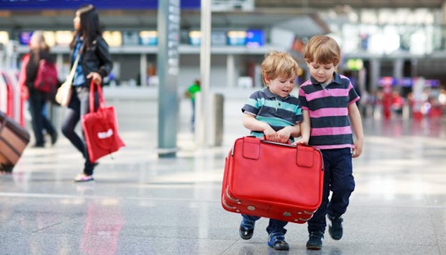 Two young boys in striped polo shirts walking around an airport, and carrying their traveling mom's ...