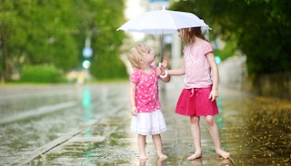Two young girls in pink clothes and no shoes holding an umbrella together in the rain