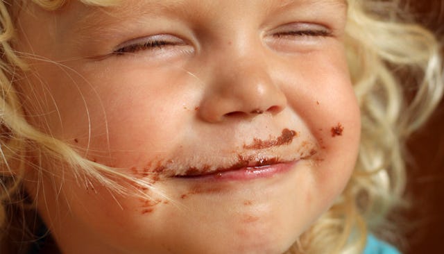 A close-up of a blonde girl smiling with closed eyes with chocolate smeared over her face