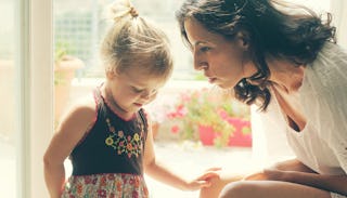 A brunette mother sitting while talking to her blonde toddler daughter