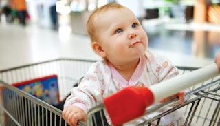 A little baby sitting in a shopping cart and holding to it tightly
