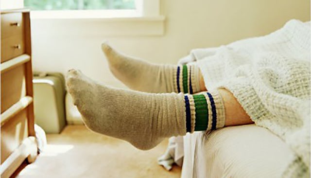 A close-up of men's feet in gray and green socks while he is lying in his bed