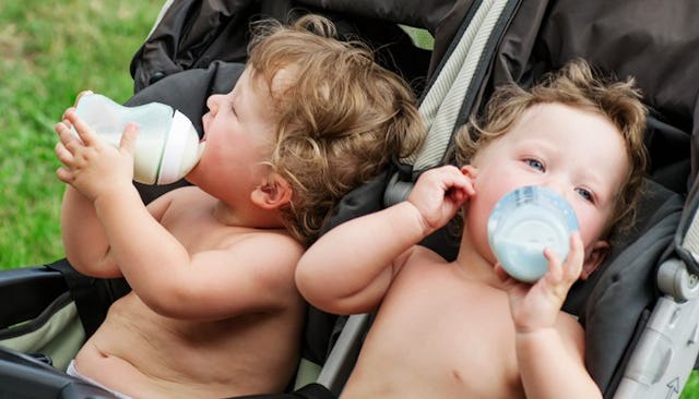 Twins drinking bottled milk in a double baby cart