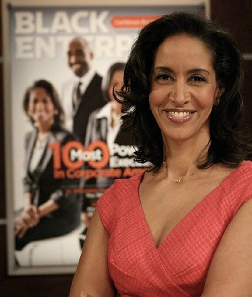 Caroline Clark in a peach-colored dress posing with the cover of Black Enterprise behind her 