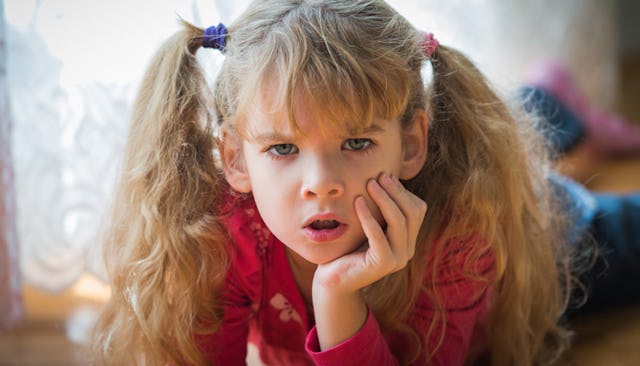 A seven-year-old blonde girl with Asperger's, lying on the floor with an angry facial expression 