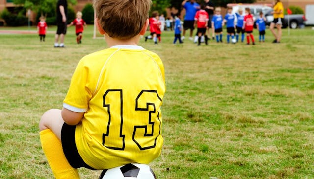 Little Boy Sitting On A Soccer Ball refusing to participate in a game