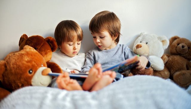 Two boys in a bed reading a little picture book surrounded with toys