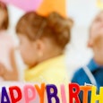Kids celebrating a half-birthday with individual multi-colored letter  birthday candles forming happ...