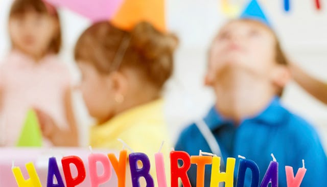 Kids celebrating a half-birthday with individual multi-colored letter birthday candles forming happ...