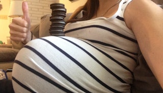 Woman taking a picture of her pregnancy stomach with Oreos stacked on top of it while showing thumbs...