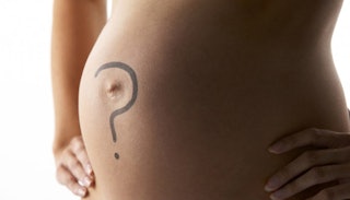 A naked pregnant woman holding hands on her hips with a black question mark drawn on her belly