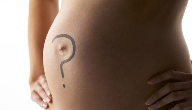 A naked pregnant woman holding hands on her hips with a black question mark drawn on her belly