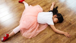 A young girl lying down on the floor in a white and pink ballerina outfit