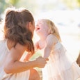 A brunette woman with tied-up hair in a white dress holding her laughing four-year-old daughter next...