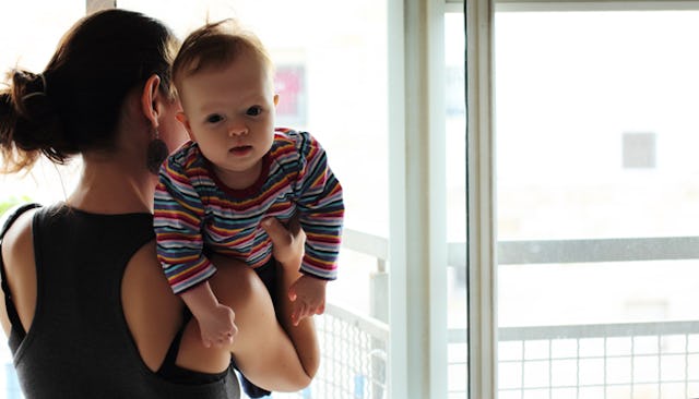 A domestic violence survivor looking through the window, holding her baby in a striped long-sleeved ...