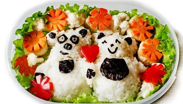 Bento food box with rice shaped like two bears and served with tomatoes and lettuce on a white plate