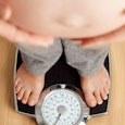 Woman with gestational diabetes standing on a scale and holding her naked stomach.