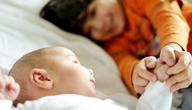 A kid holding baby's hand as they're both lying on a bed